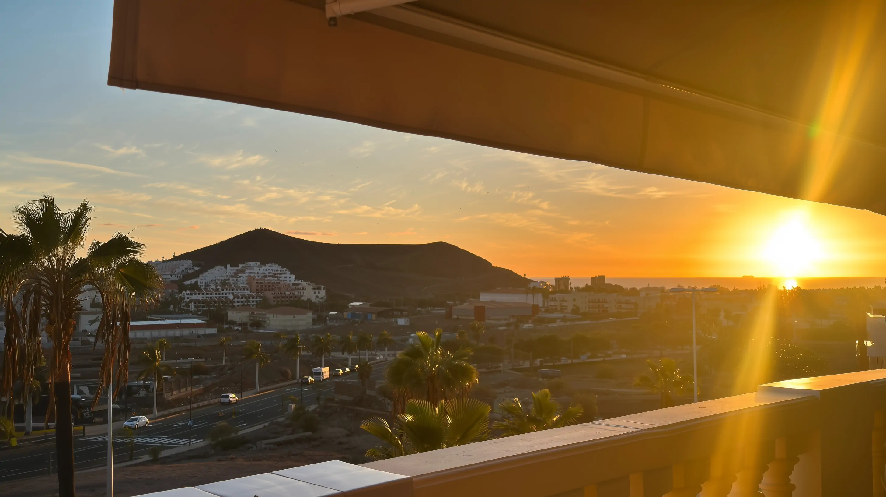 Zachód słońca nad południową Teneryfą widziany z balkonu, palmy i zabudowa w ciepłym świetle