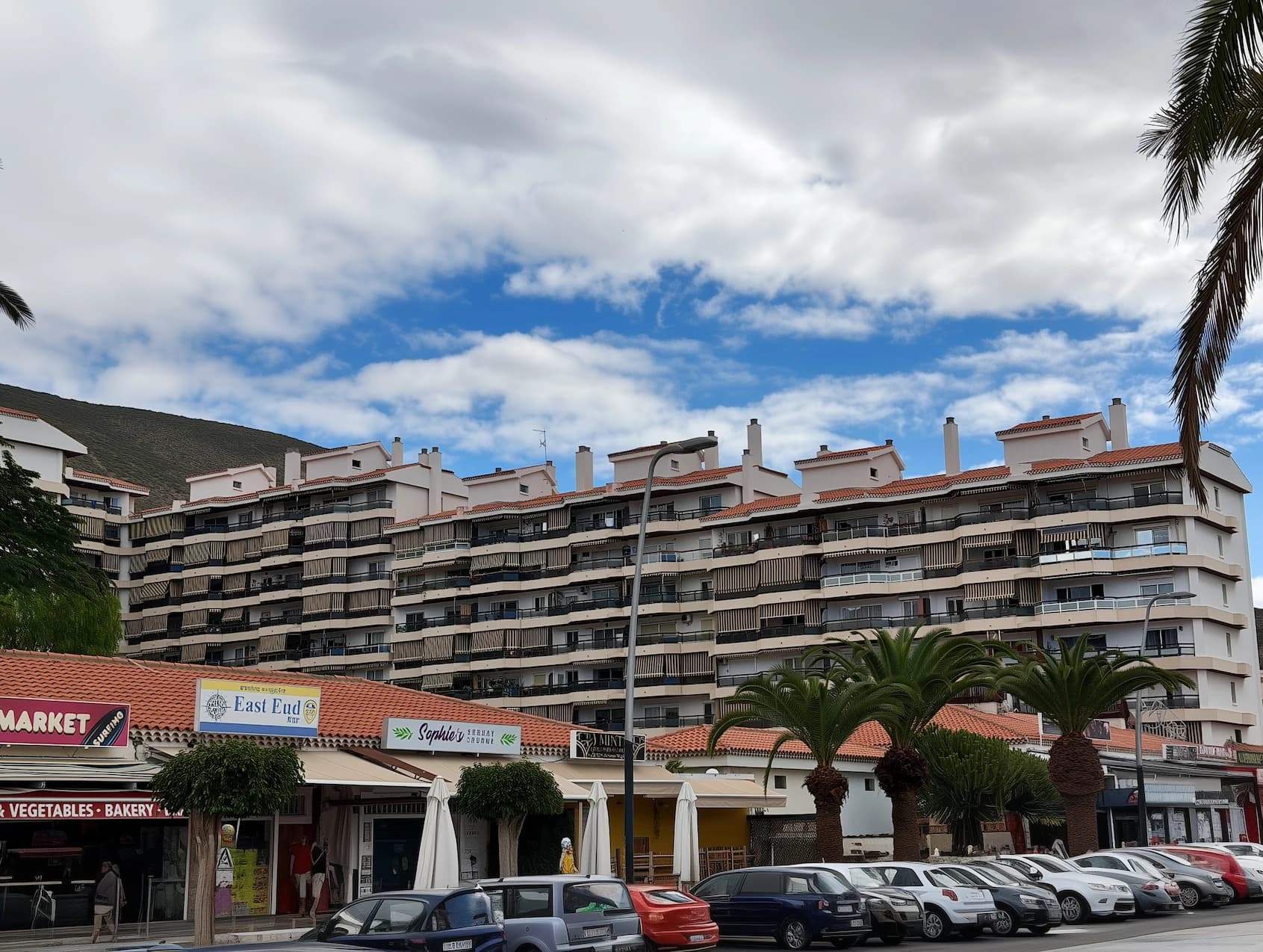 Duży budynek apartamentowy na Teneryfie z lokalami usługowymi na parterze i niebieskim niebem w tle