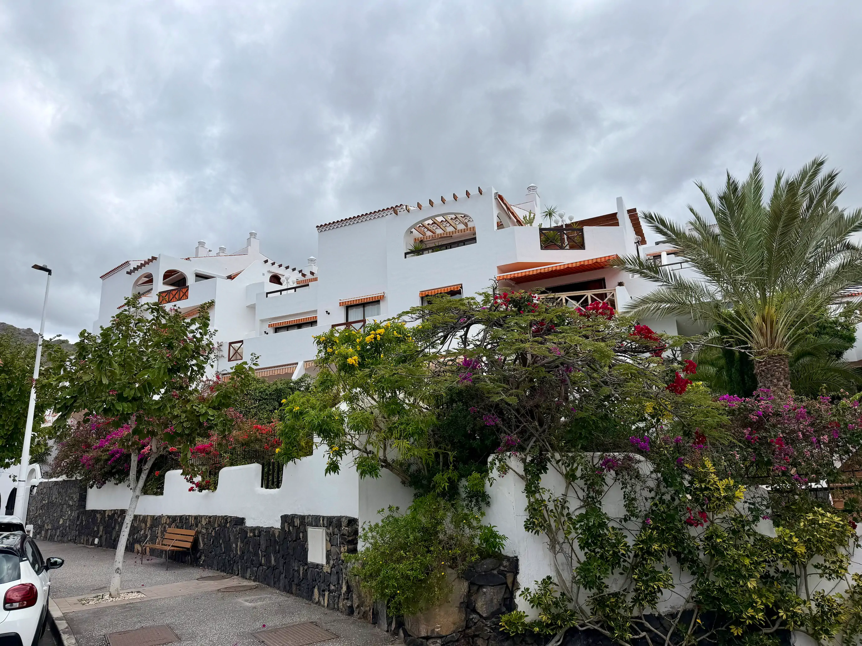 Urocze białe apartamentowce na Teneryfie otoczone kwitnącą bugenwillą i palmami