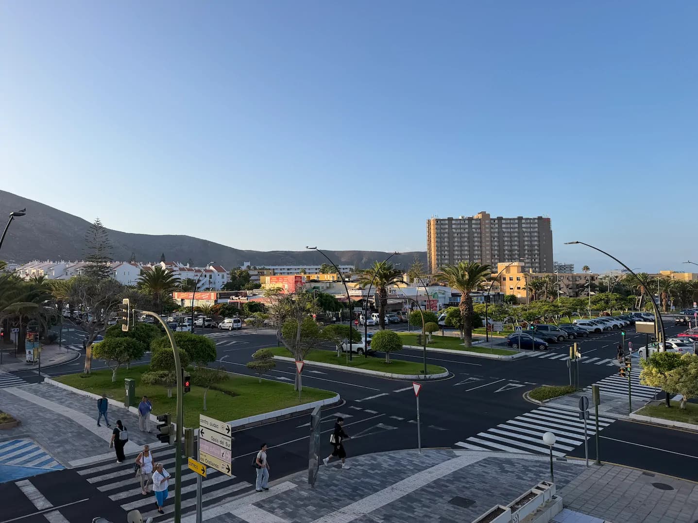Poranek na Avenida Juan Carlos I w Los Cristianos – szeroka aleja z zielonymi pasami, przejściami dla pieszych i wzgórzami w tle