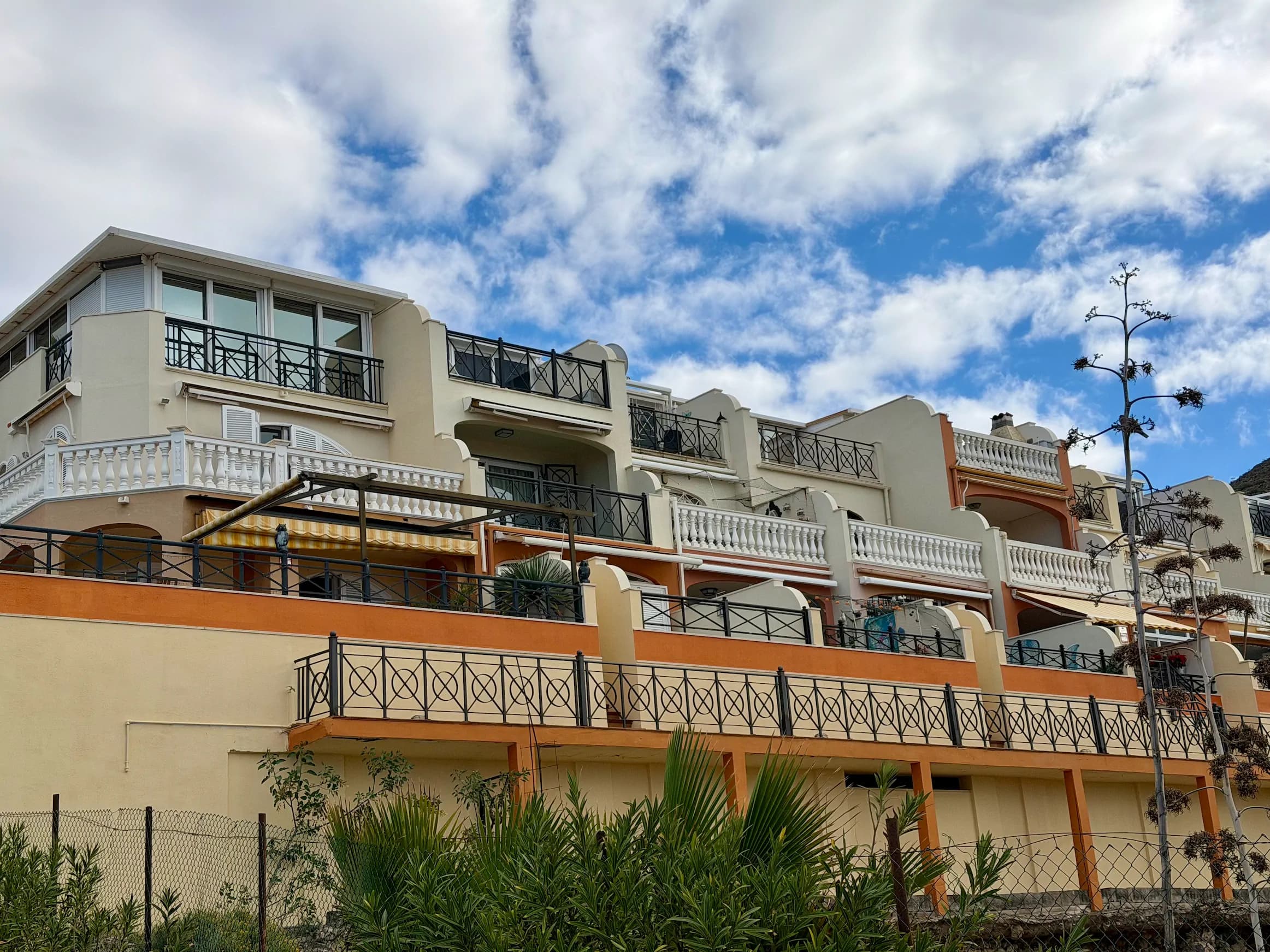 Białe domy szeregowe w zabudowie kaskadowej na wzgórzu z dużymi tarasami i markizami na tle błękitnego nieba