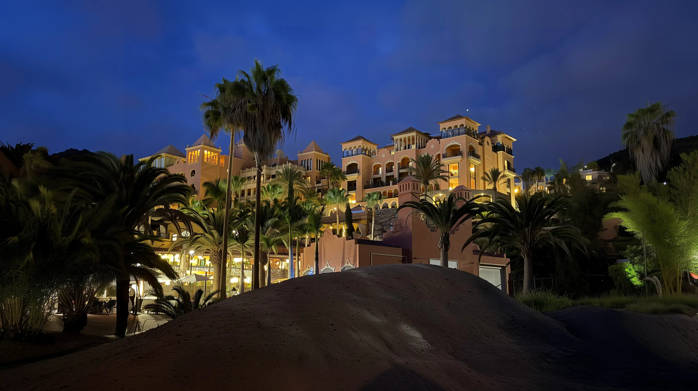 Luksusowe hotele i apartamenty w okolicy Playa del Duque nocą, ciepłe oświetlenie, palmy