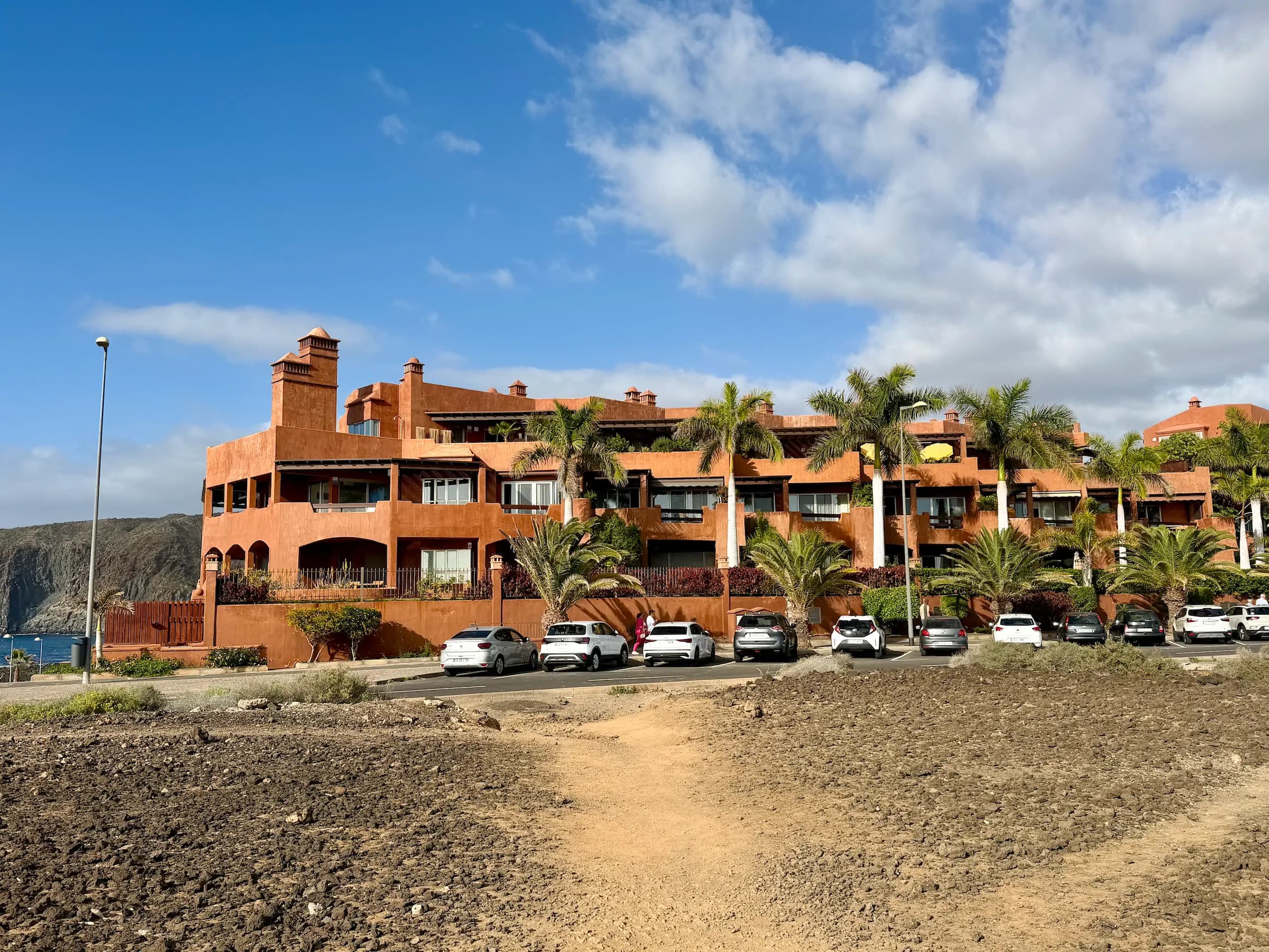 Ceglasty budynek apartamentowy w stylu rezydencjalnym z kaskadowymi tarasami i palmami na tle błękitnego nieba