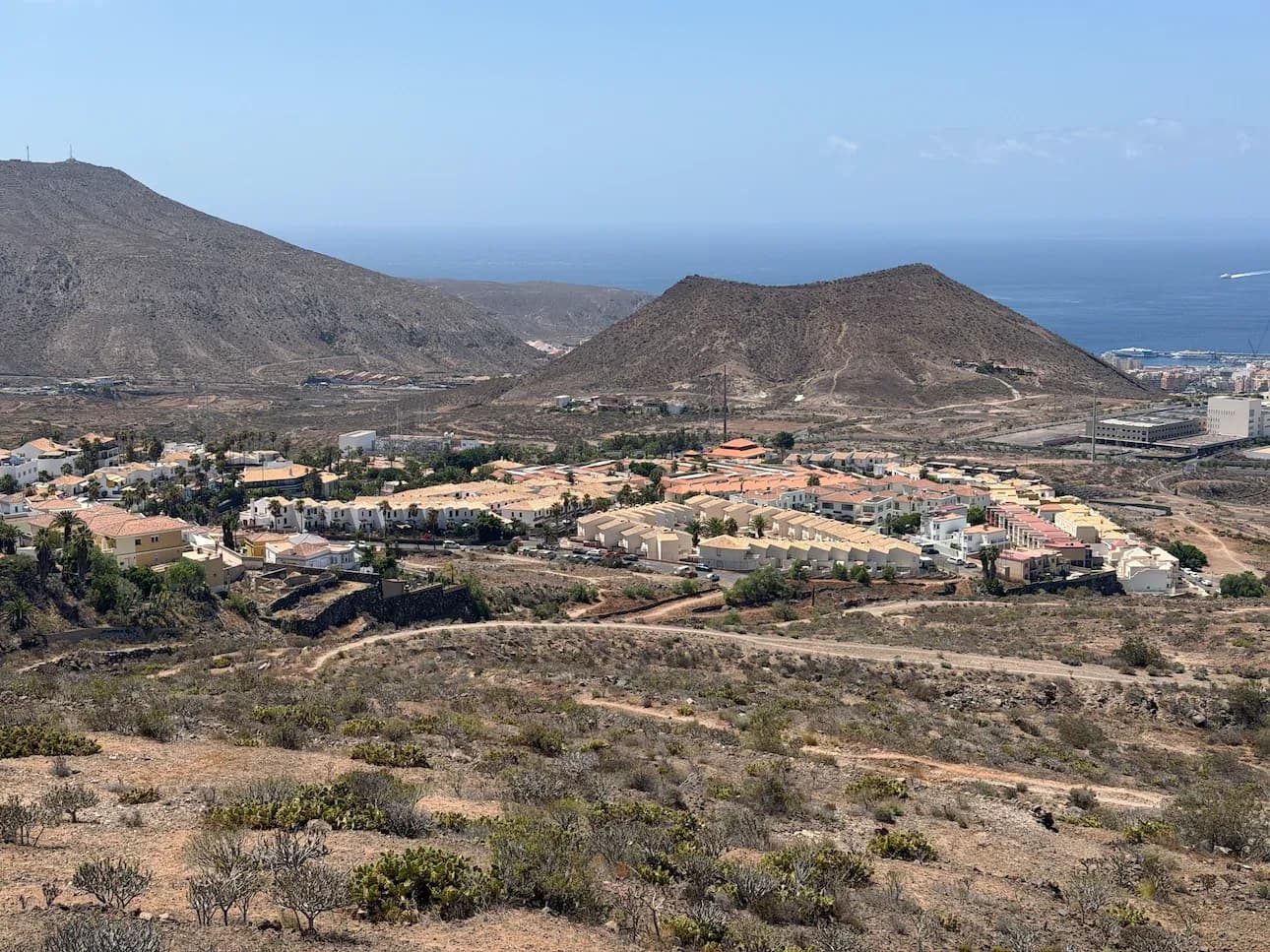 Widok ze wzgórza nad Chayofą w gminie Arona na osiedle domów z basenami, wulkaniczne wzgórza i ocean z portem Los Cristianos w tle