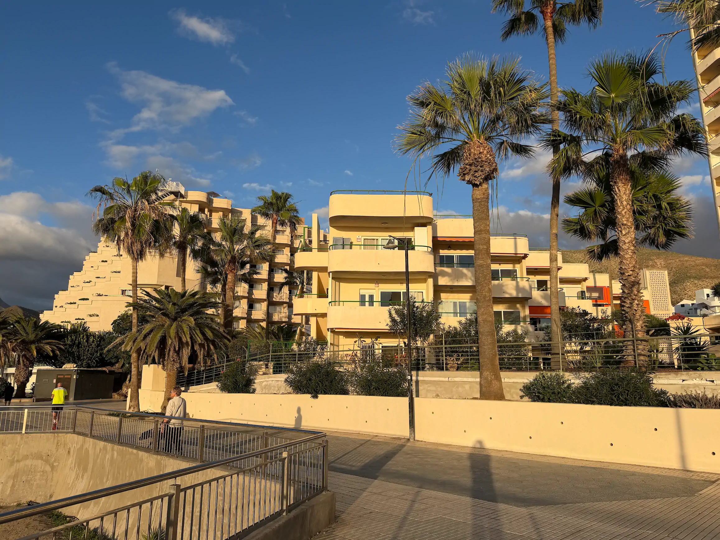 Budynek apartamentowy w kolorze terakoty z białymi balkonami i ogródkami na parterze otoczonymi zielenią