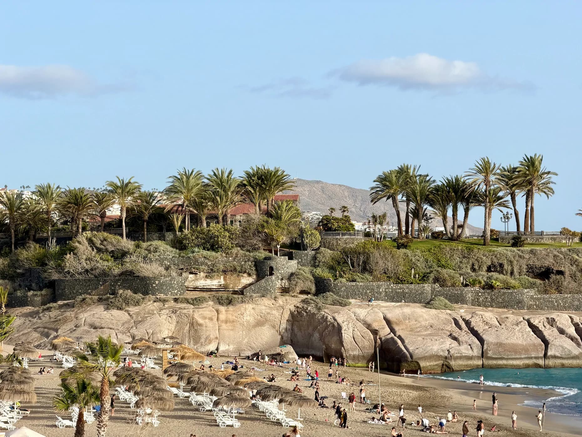 Plaża Playa del Duque na Teneryfie z widokiem na luksusowe wille na klifie i słomiane parasole