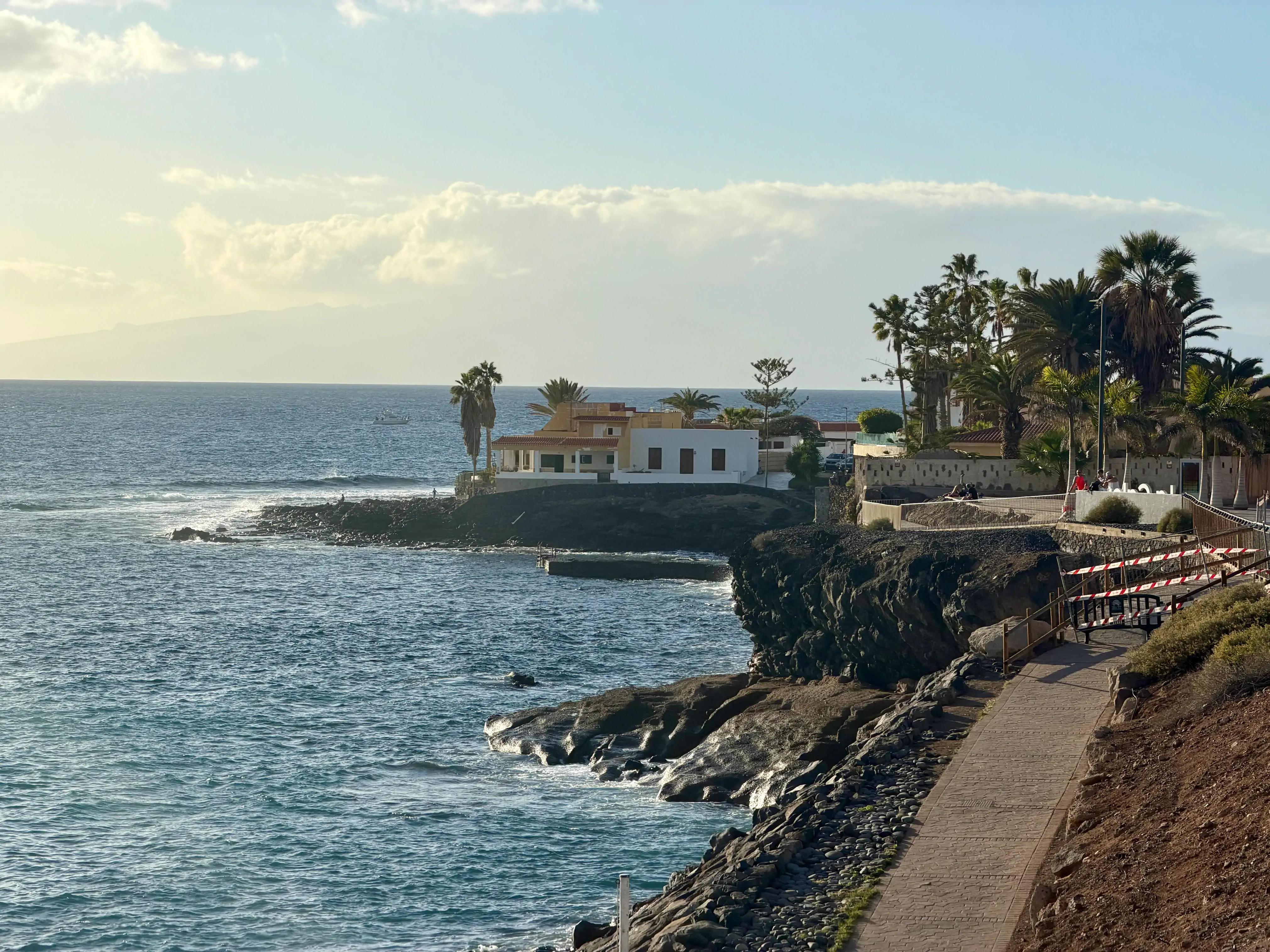 Promenada nad oceanem na Teneryfie o zachodzie słońca, w tle białe domy i wyspa La Gomera