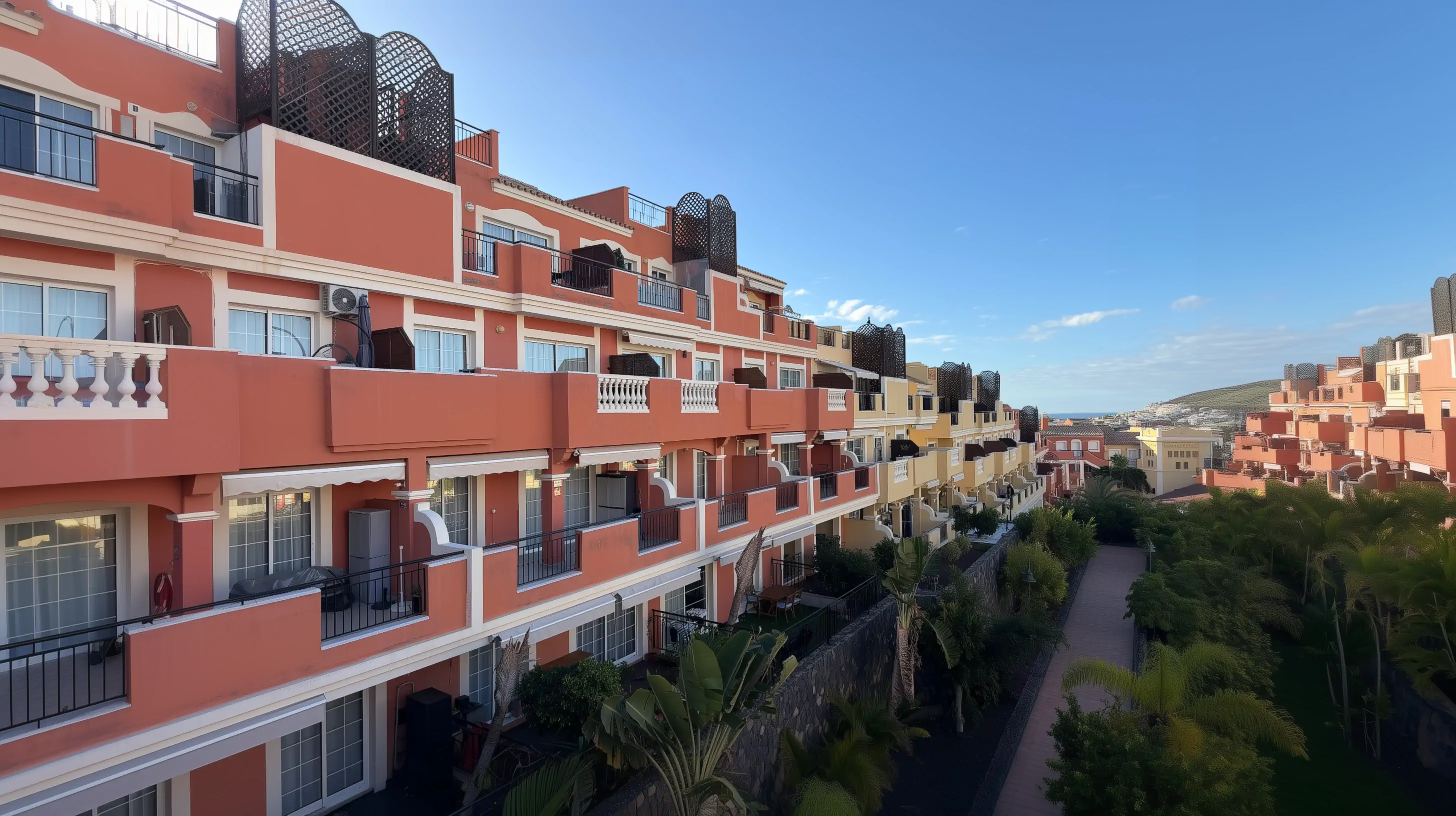 Kolorowe apartamentowce na Teneryfie z dużymi tarasami i palmami w ogrodzie