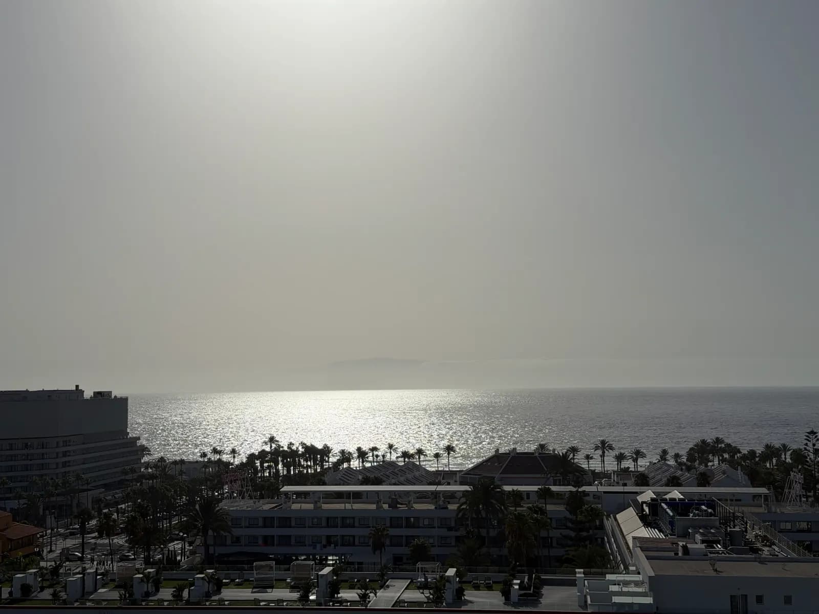 Widok z wysokiego balkonu przy Calle de California w Playa de las Américas na palmy, hotele i ocean z La Gomerą na horyzoncie