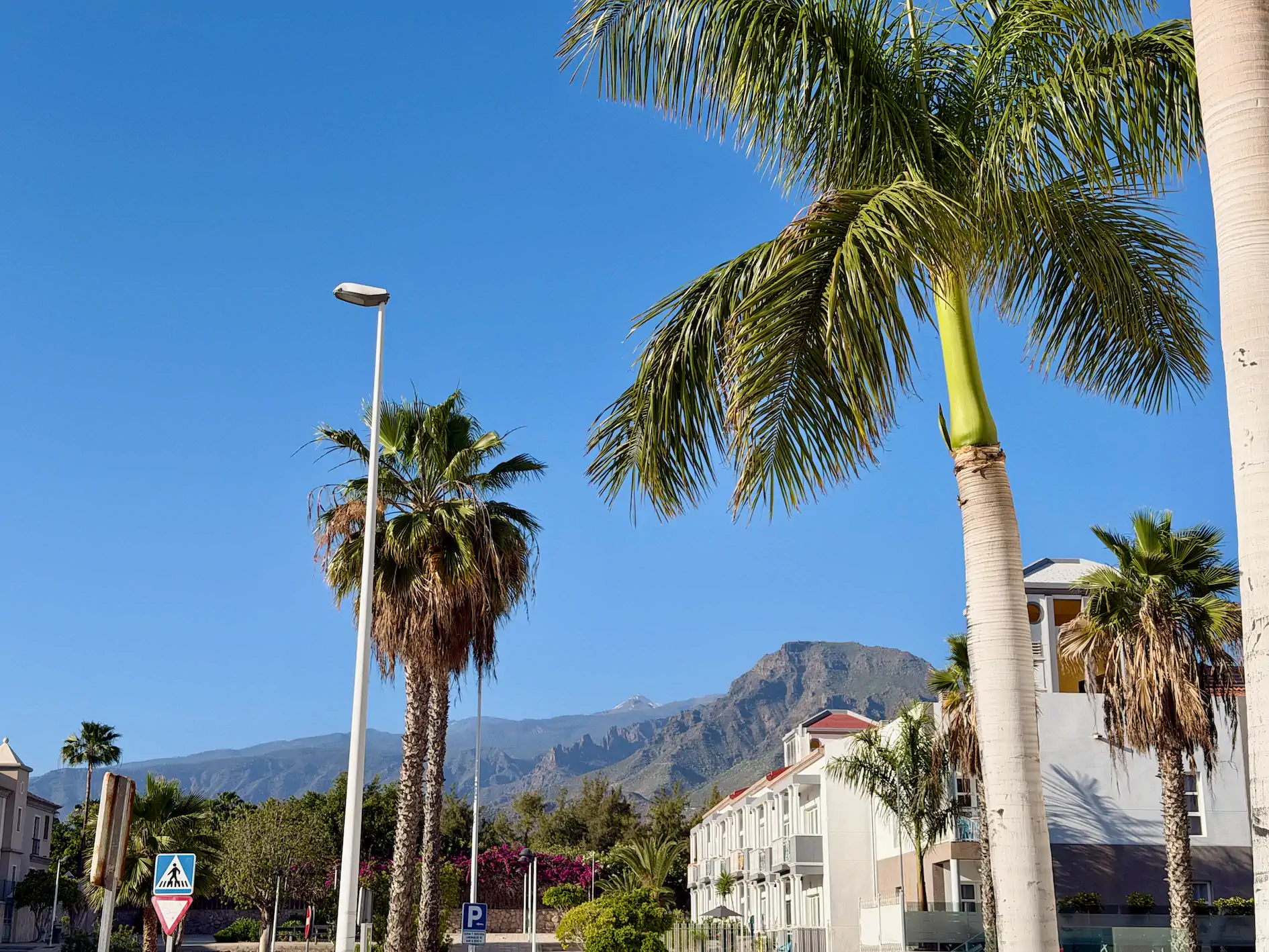Luksusowy taras ze szklaną balustradą, kolorowe osiedle w dole i ośnieżony wulkan Teide w tle
