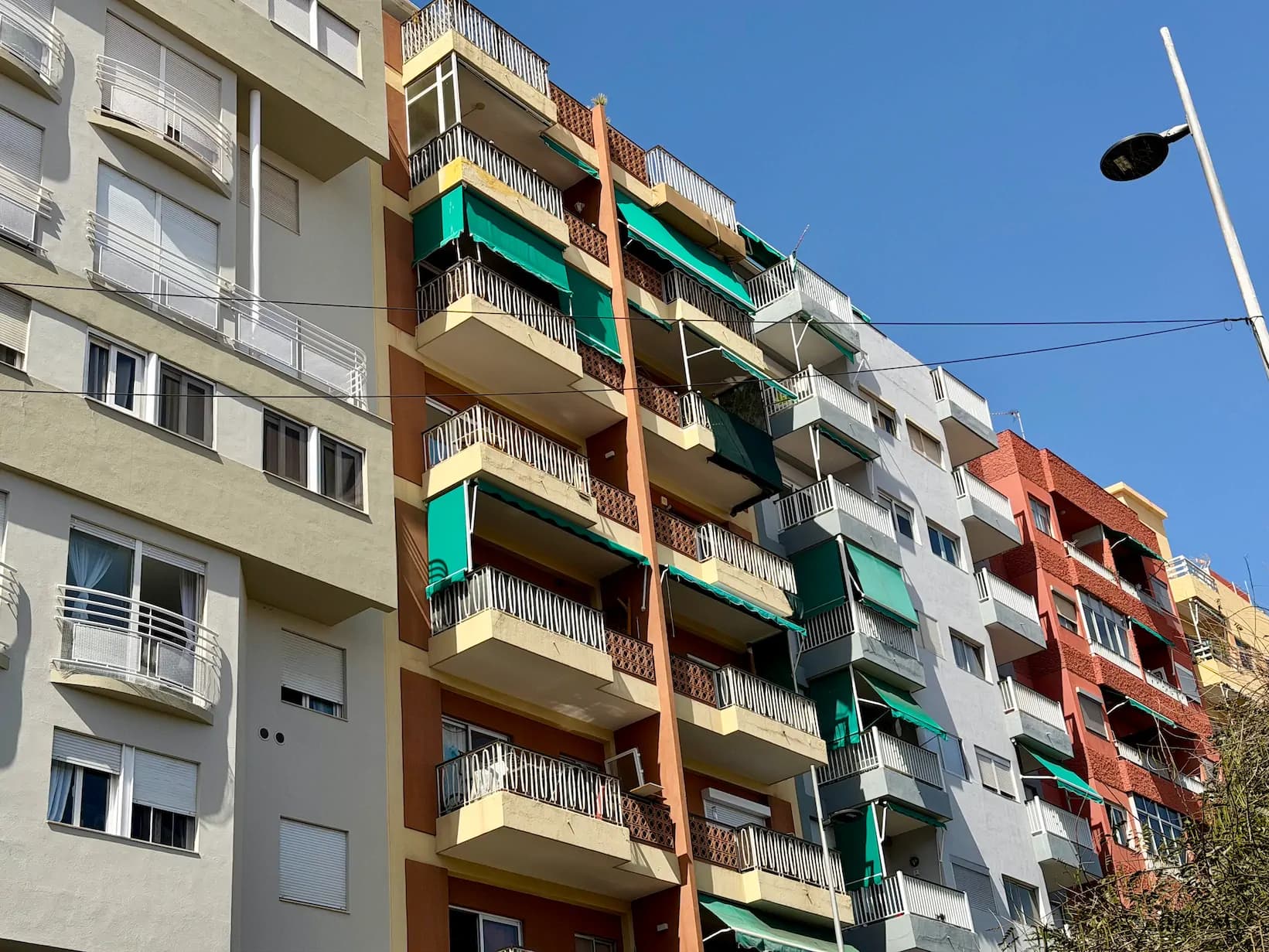 Wielokolorowe fasady hiszpańskich bloków w Santa Cruz de Tenerife z charakterystycznymi, opuszczonymi zielonymi markizami