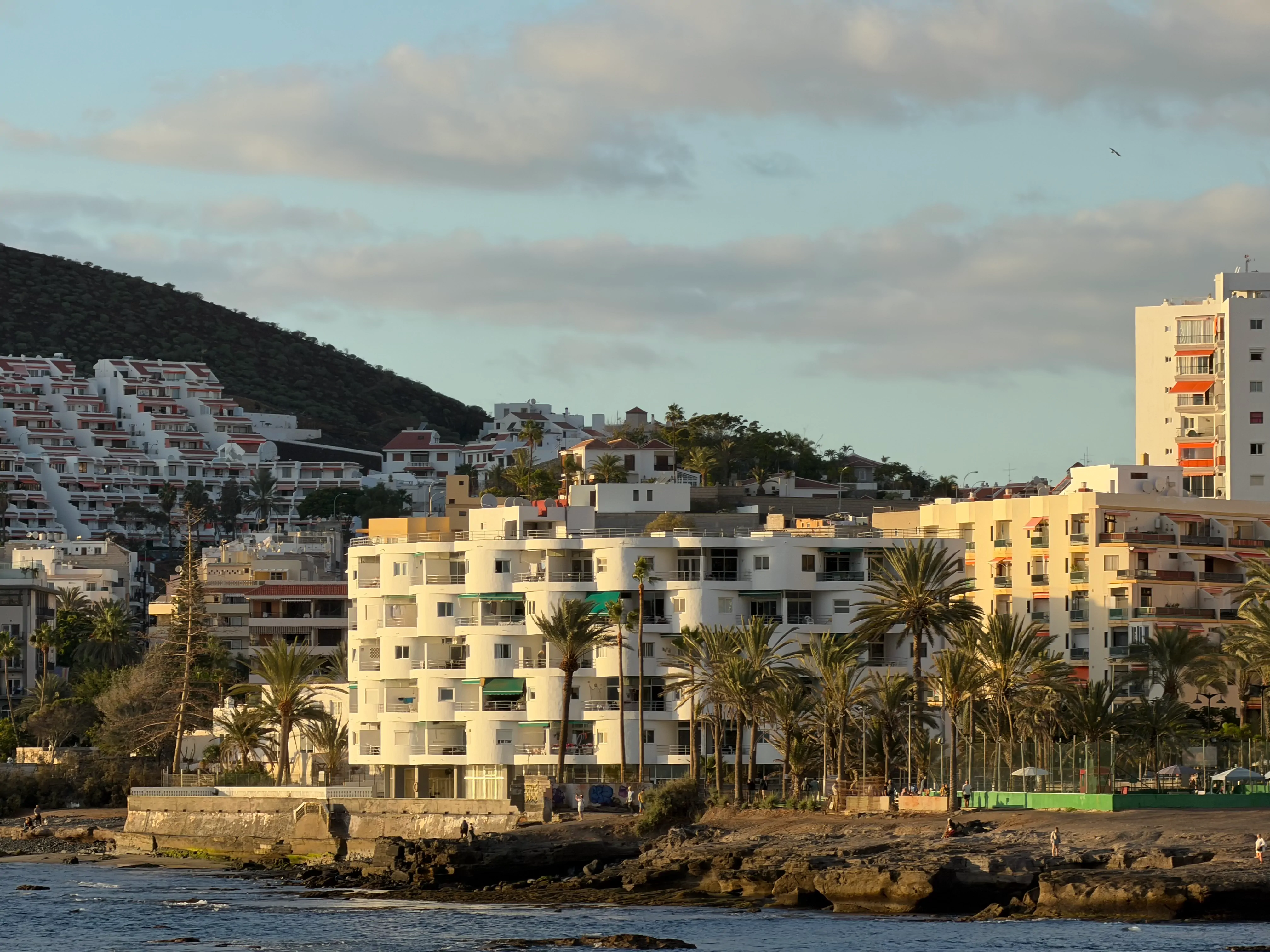 Wybrzeże Teneryfy z białym zaokrąglonym apartamentowcem na pierwszym planie i kaskadową zabudową na wzgórzu w tle