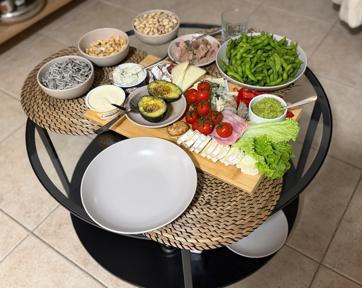 Szklany stół z przekąskami: awokado, pomidorki koktajlowe, edamame, sery, orzechy i nasiona